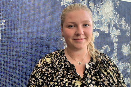 Linn Eriksson, nyanställd GIS-ingenjör framför blå mosaikvägg