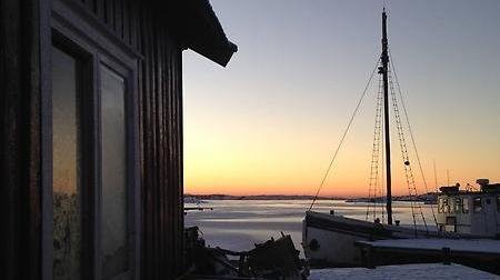 Utblick från brygga med sjöbod och fiskebåt i solnedgången en vinterdag i Väjern.