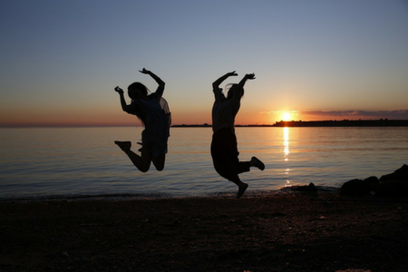 Silhuett av två personer som hoppar på en strand i solnedgång.