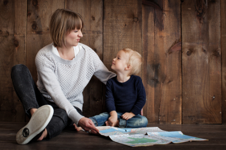 Kvinna sitter med ett barn på ett golv och de tittar på varandra och ler. Framför sig håller de ett papper.