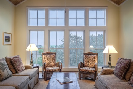 Rum med två soffor och två fåtöljer samlade runt ett soffbord, med stora fönster i bakgrunden.