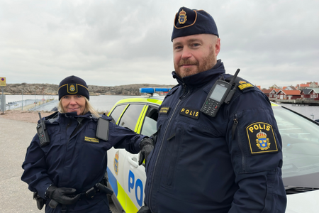En kvinnlig och en manlig polis framför en polisbil på Väjern