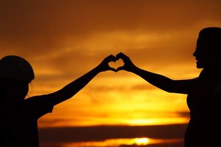 Silhuett av två personer som håller händerna som ett hjärta med solnedgång i bakgrunden.