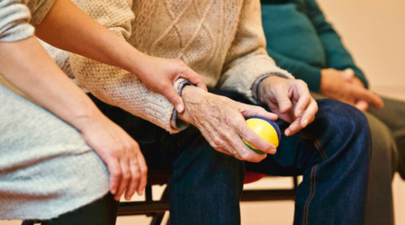 Yngre person håller äldre persons armled, den äldre personen håller i en liten boll.