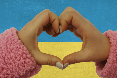 En flickas händer bildar ett hjärta, i bakgrunden syns Ukrainas flagga.