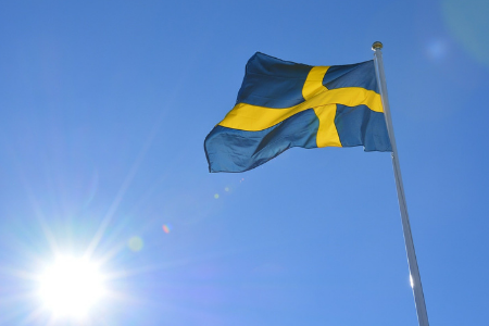 En flagga i gult och blått vajar i vinden, i bakgrunden syns solen skina starkt.