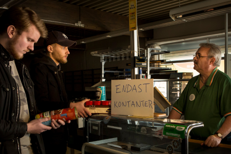 nedsläckt affär med skylten bara kontanter två män försöker handla konserver av en annan man som ser uppgiven ut.